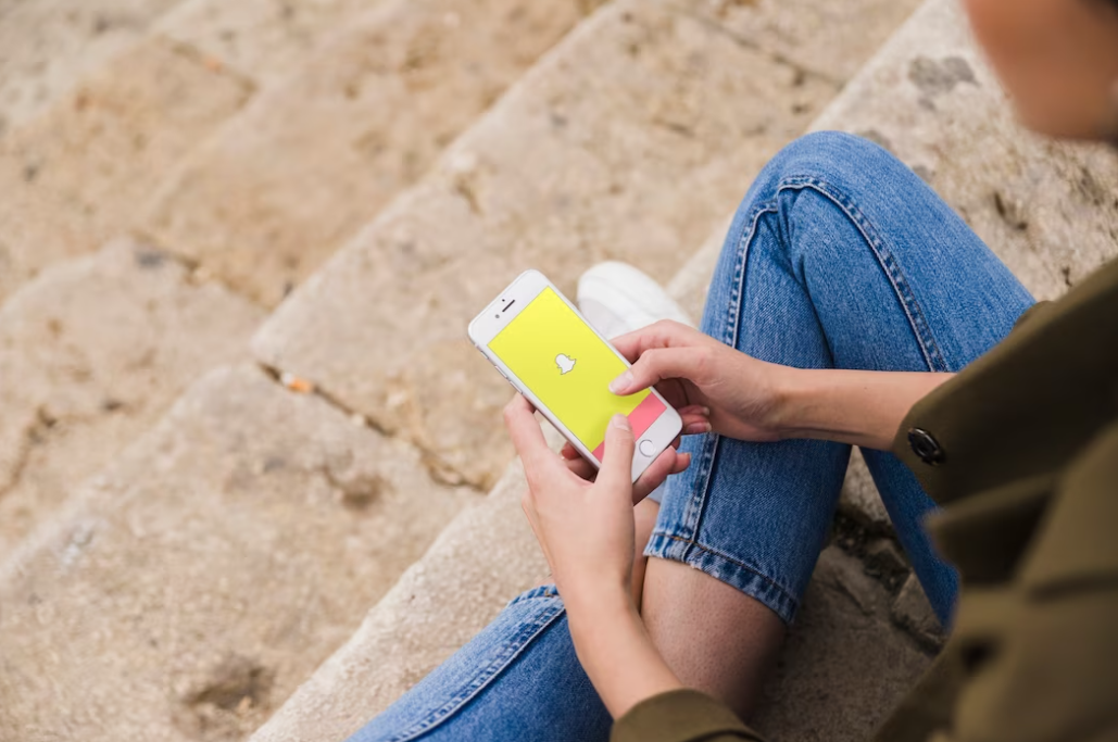 woman sitting on the stairs outside and holding the smartphone with Snapchat on it