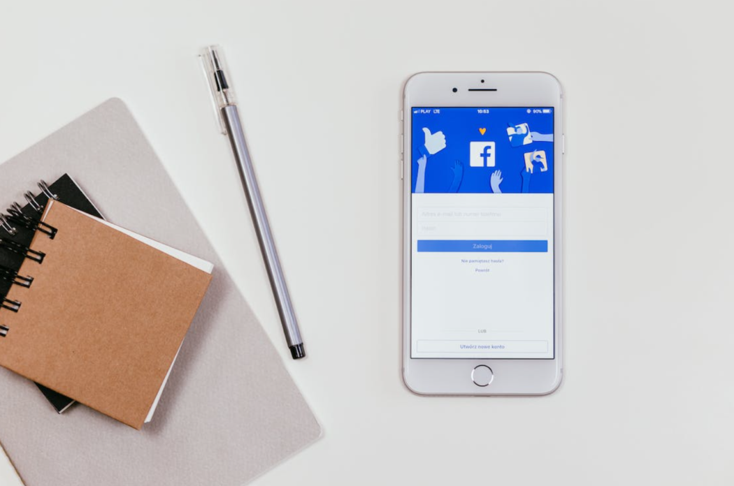 phone with facebook platform on it, notebooks and pen on the white table